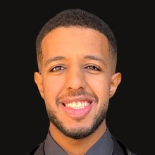 Portrait of Abdelrahman Abdalla Mohamed, a smiling man with short dark hair and a beard, wearing a dark suit and a stethoscope.